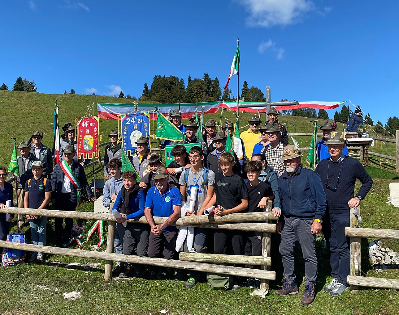 Gruppo di alpini e civili davanti al cippo con gli stendardi della 44ª e della 24ª batteria e il tricolore